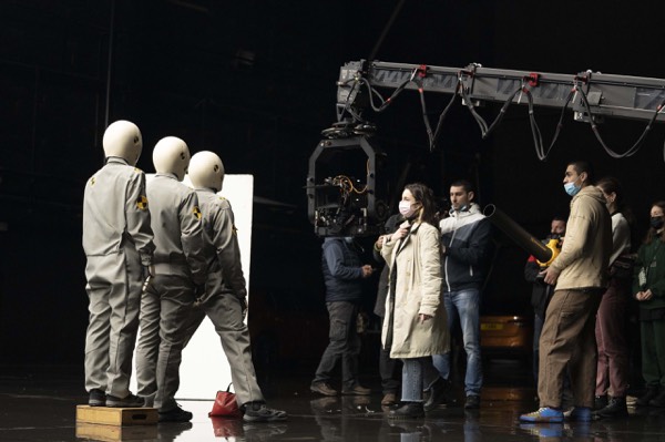 Figures in white suits and a camera in a sound stage