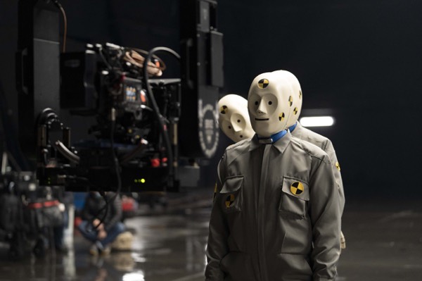 Camera and actors in white suits in a dark studio