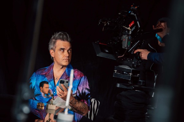 Performer in a patterned shirt and a camera behind the scenes
